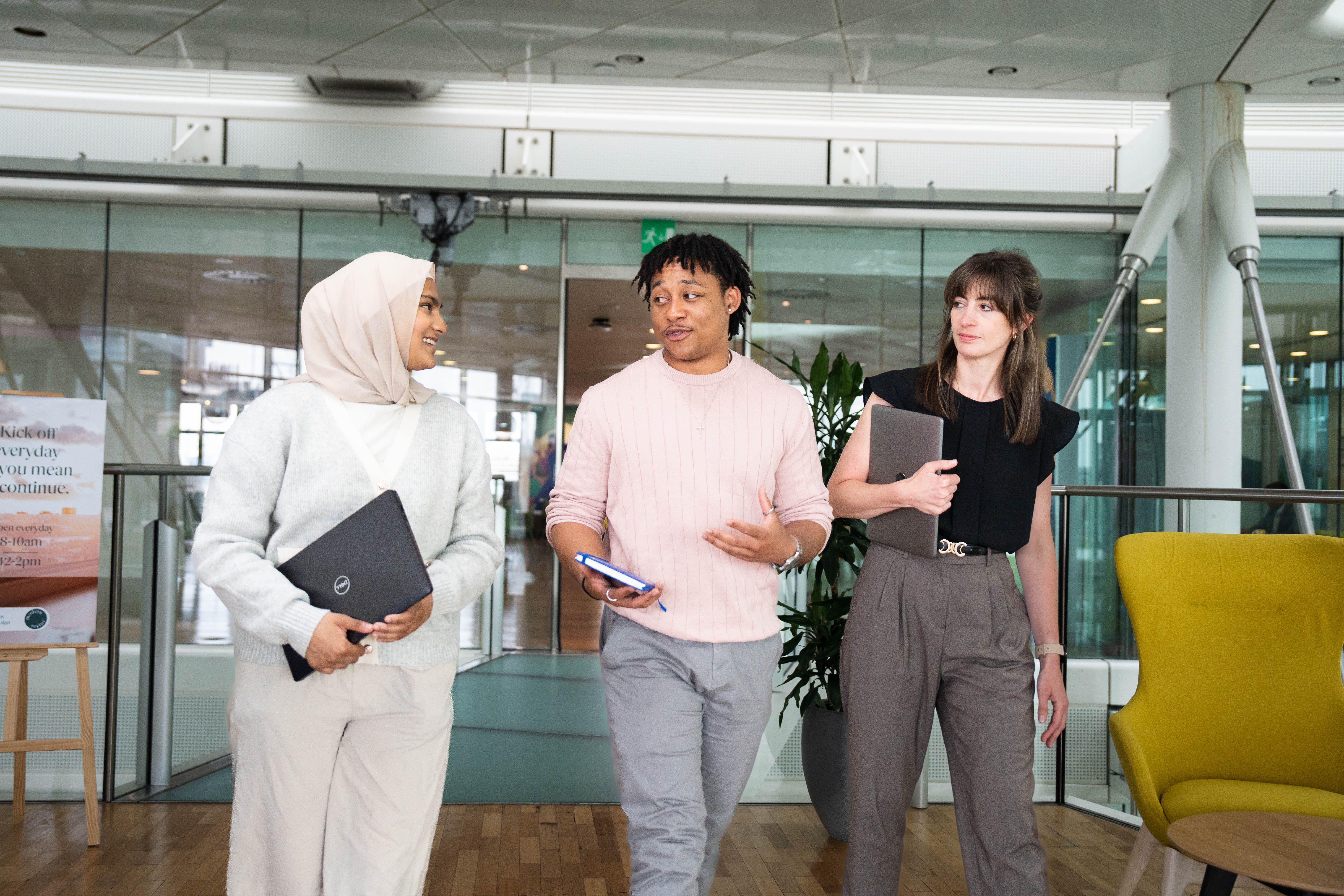 Three individuals walking and conversing in a modern office space. 